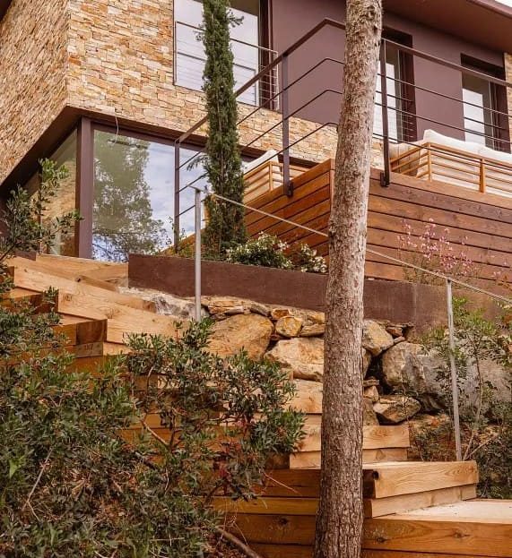 Внешний фасад виллы с натуральной каменной отделкой и лестницей среди сосен.