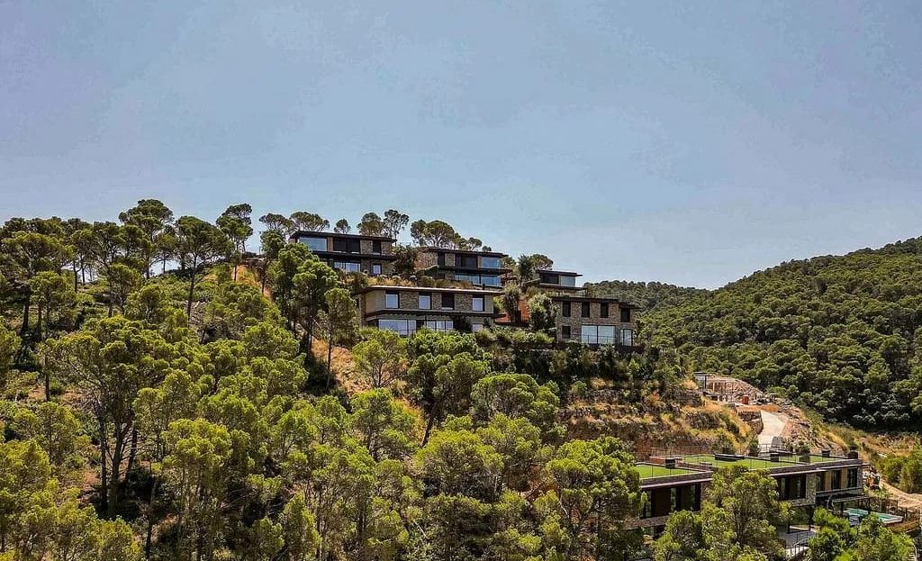 Вид на жилой комплекс вилл среди соснового леса на склоне холма.