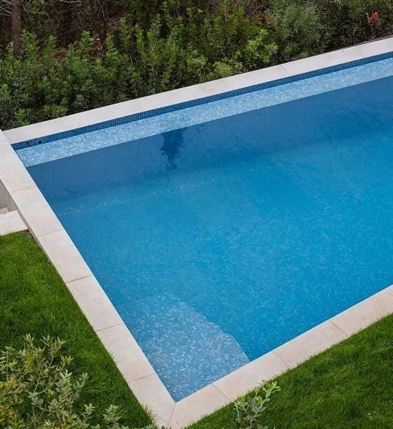 Частный плавательный бассейн с голубой водой, окружённый зелёной зоной.