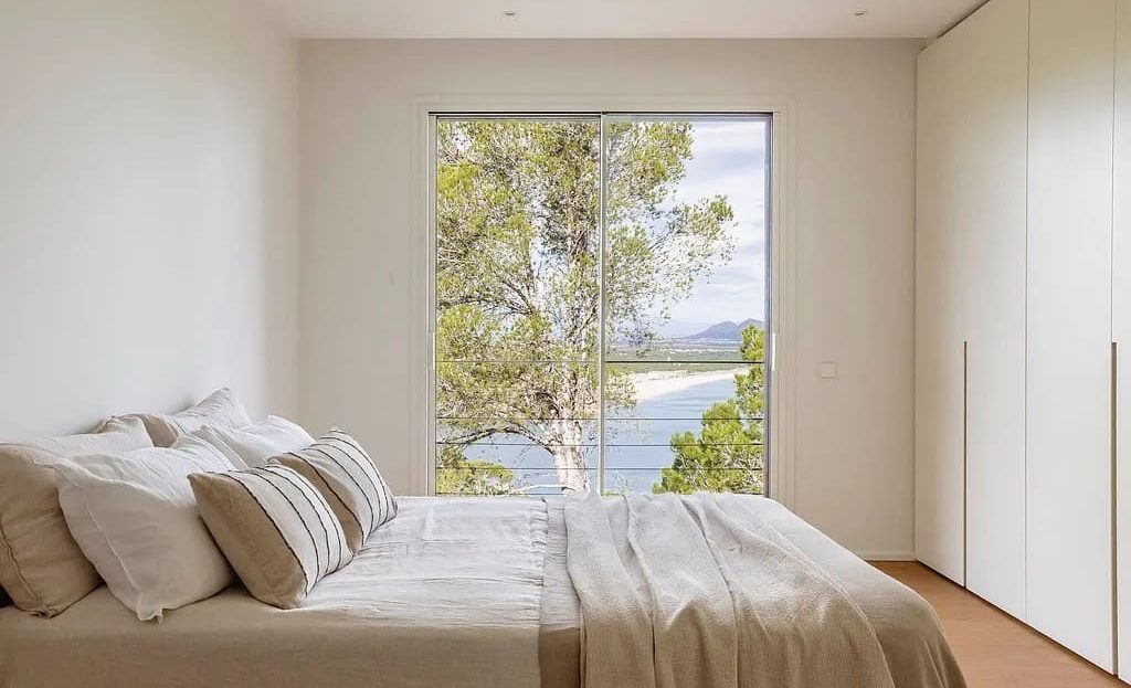 Спальня с большой кроватью и панорамным окном с видом на море и природу.