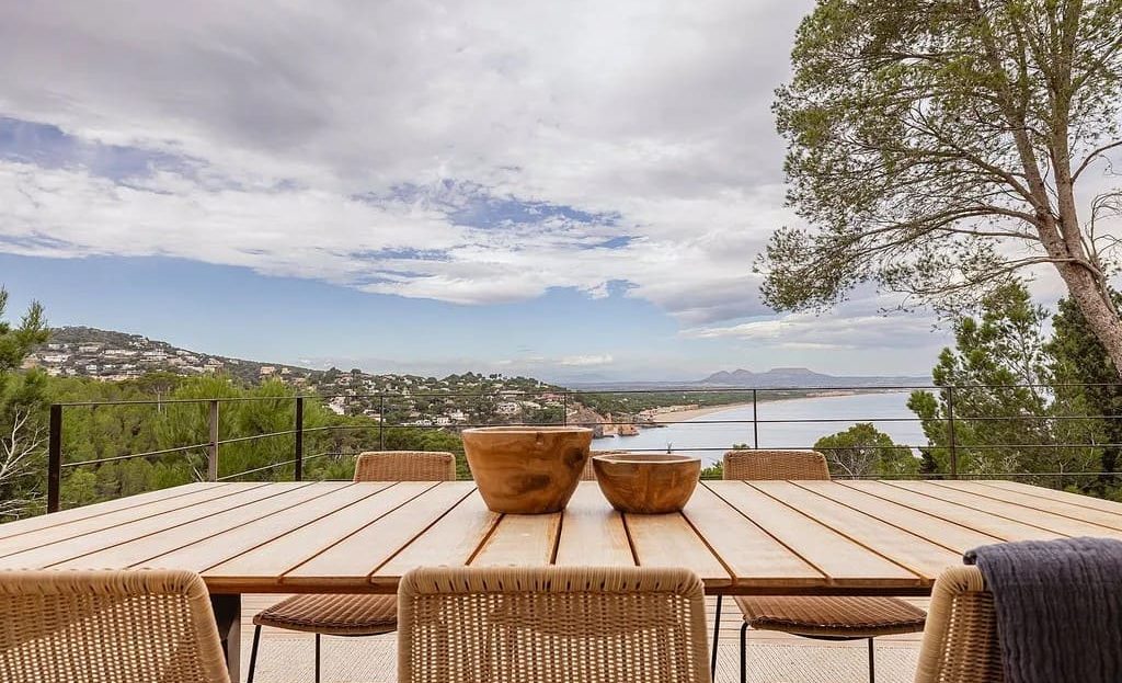 Терраса с обеденной зоной и видом на море и зелёный холмистый ландшафт.