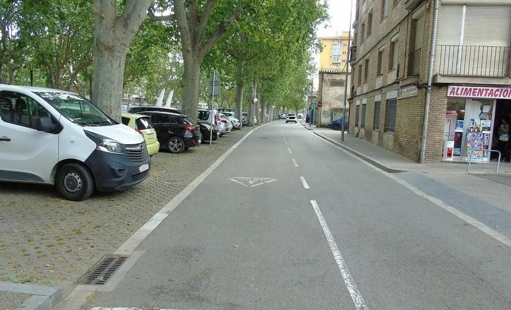 Улица с парковочными местами и высокими деревьями рядом с жилыми домами в районе El Sucre–Universitat, Vic.