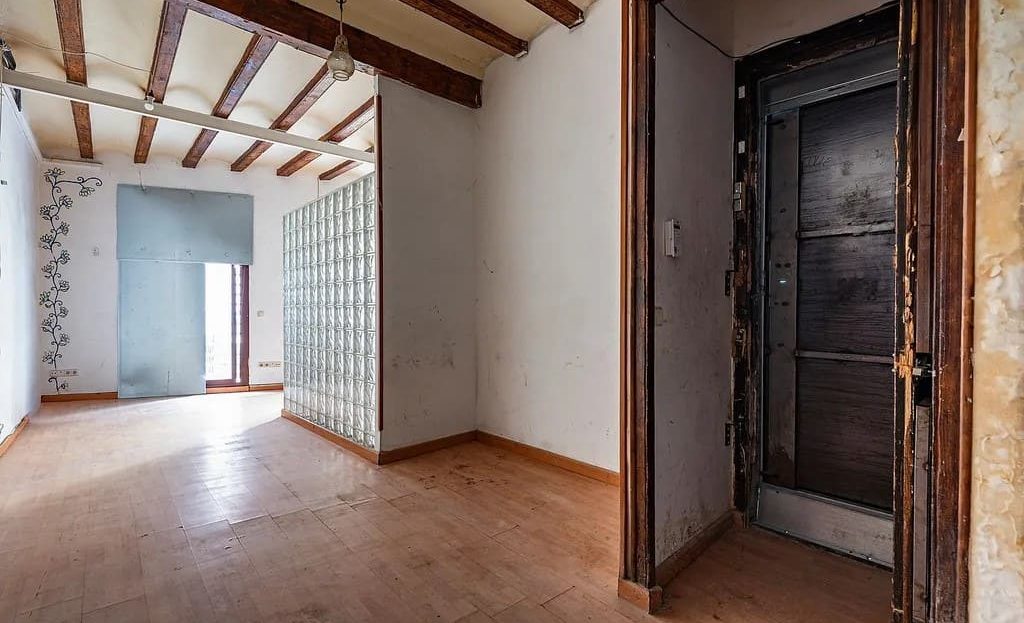 Жилая комната под реконструкцию с деревянными балками и входной дверью