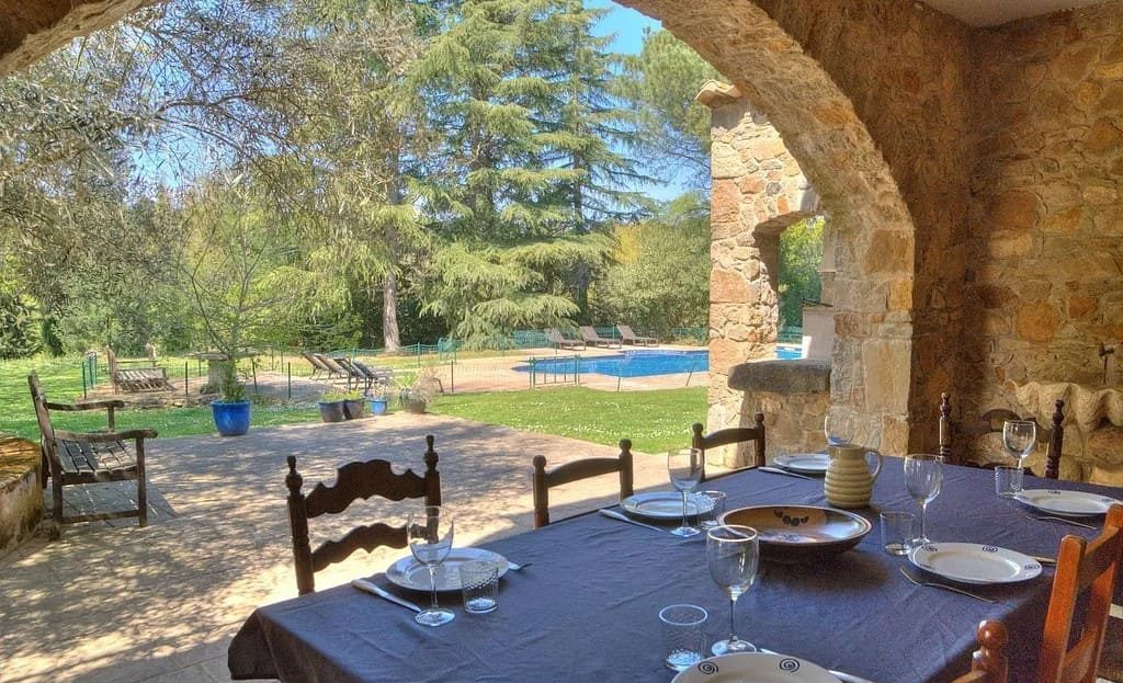 Летняя столовая под каменным арочным навесом с видом на сад усадьбы.