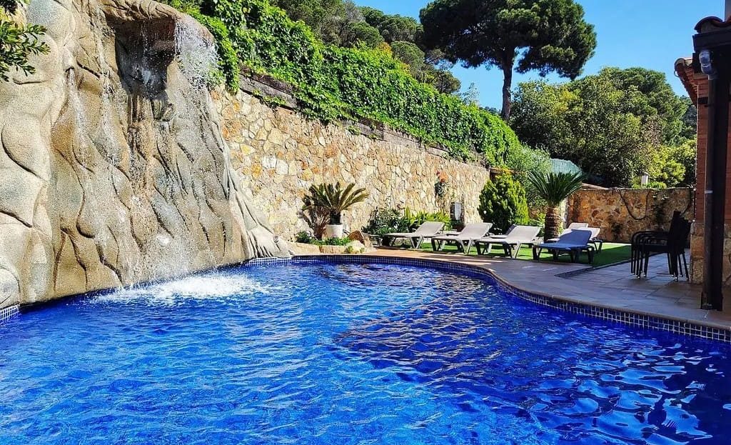 Бассейн у дома с природной каменной стеной