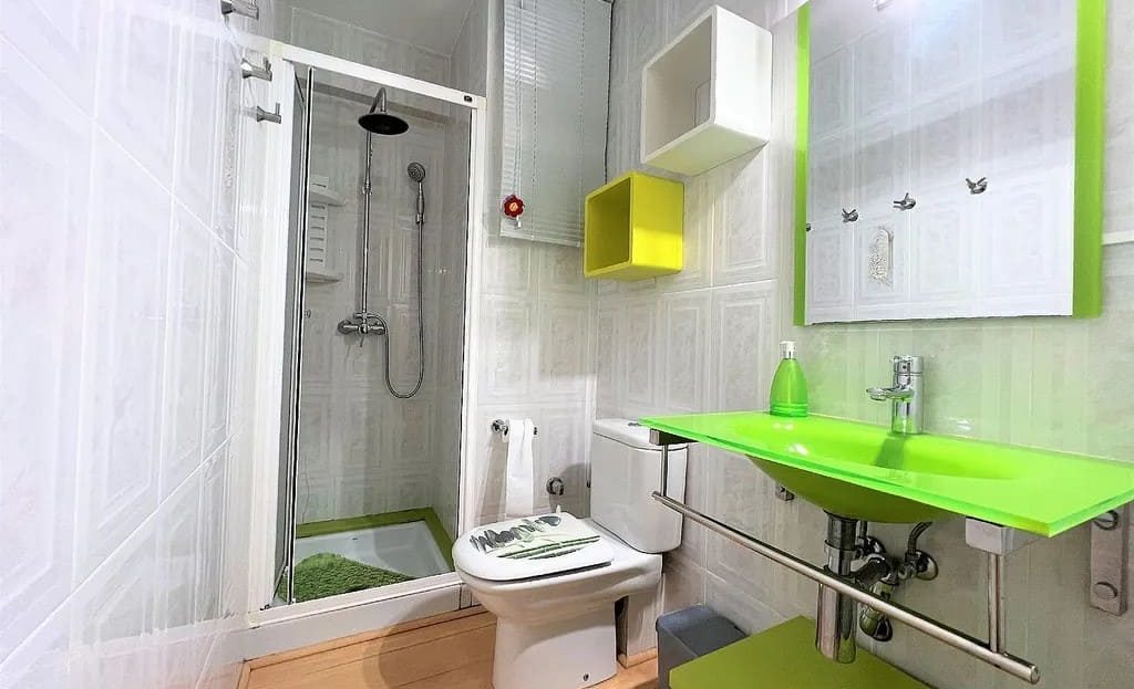 Ванная комната с душевой кабиной, унитазом и яркими зелеными элементами