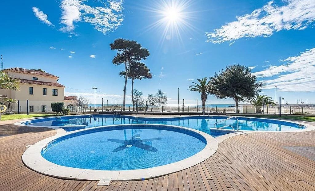 Круглый бассейн с деревянной террасой и видом на набережную.