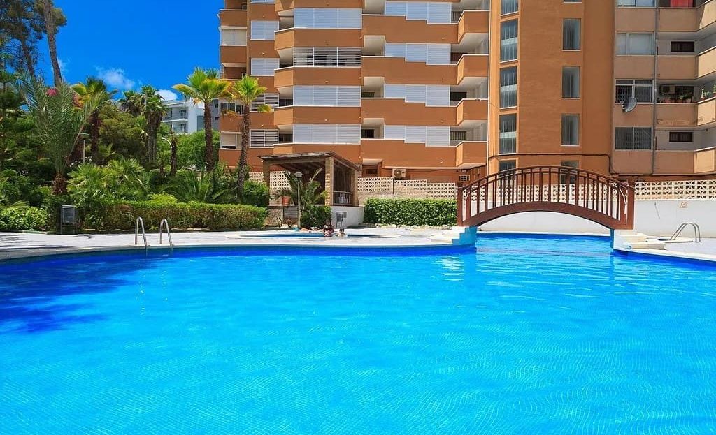 Большой бассейн с мостиком и зелёными насаждениями в жилом комплексе.