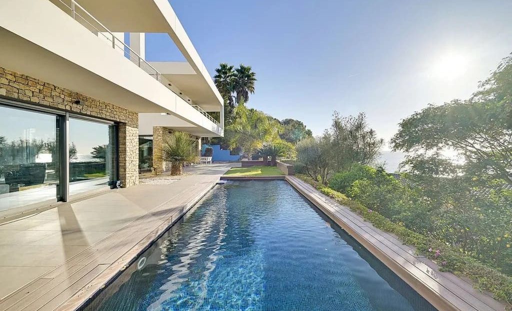 Длинный бассейн инфинити с видом на море и современной виллой