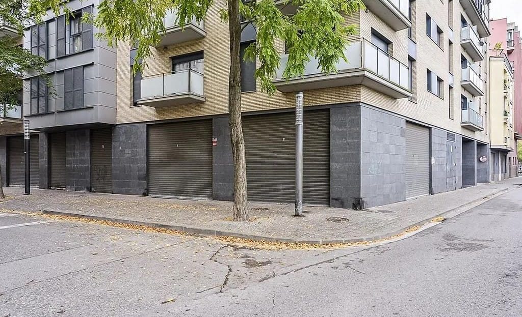 Фасад здания с закрытыми коммерческими помещениями и деревьями вдоль улицы