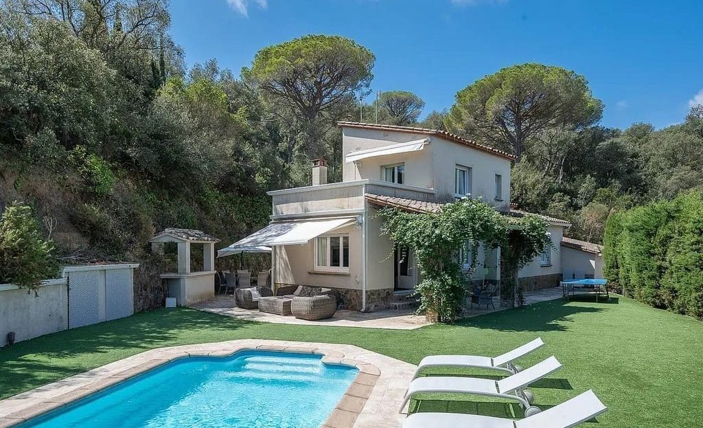 Фасад виллы с бассейном и зелёным садом.