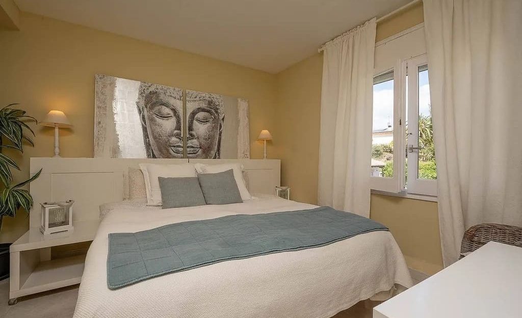 Спальня с двуспальной кроватью и большими окнами.