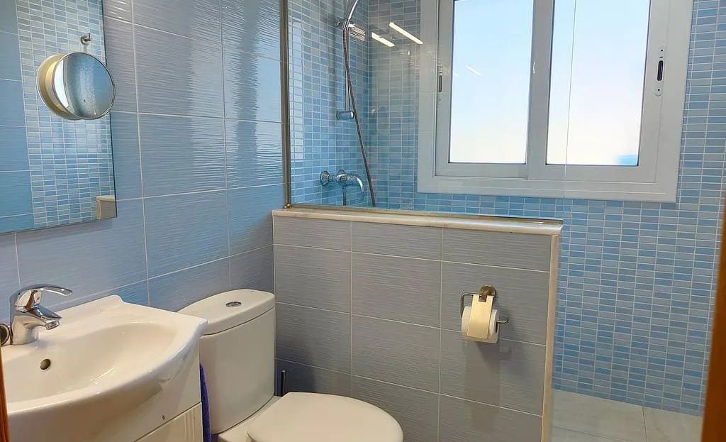 Ванная комната с душем и светло-голубой плиткой.