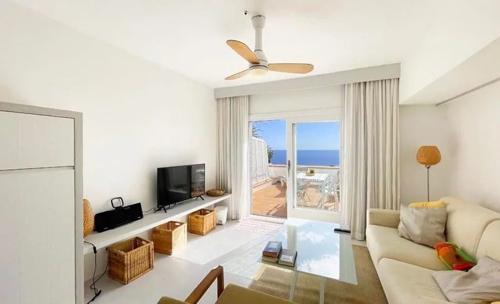 Гостиная с диваном, телевизором и выходом на террасу с видом на море.