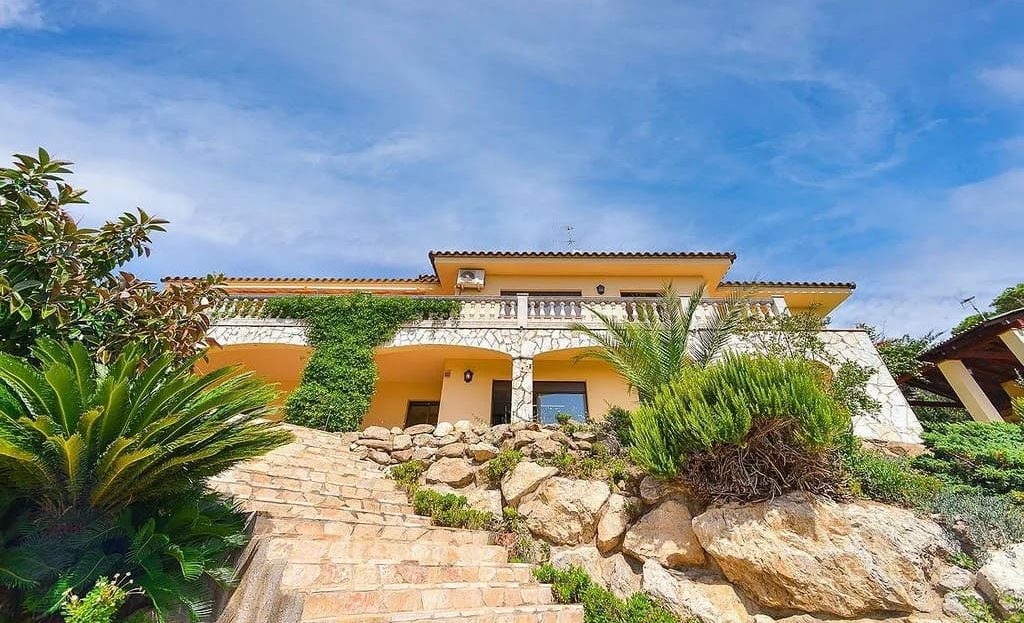 Фасад виллы с подъездной дорожкой и зелёным участком.