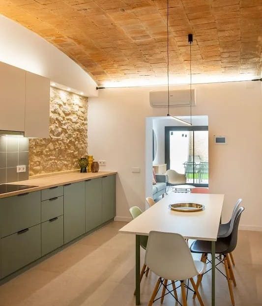 Кухня и обеденная зона с выходом света из окна и декоративной каменной стеной.