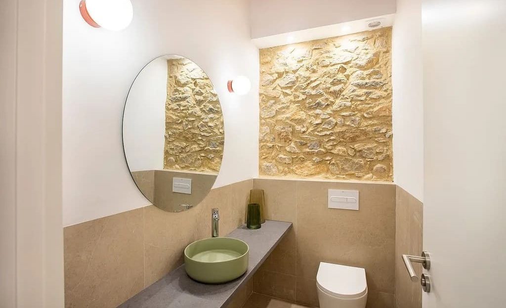 Современная ванная комната с круглым зеркалом и каменной отделкой.