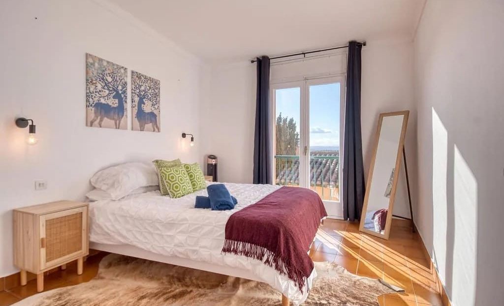 Спальня с двуспальной кроватью, большим окном и мягким освещением.