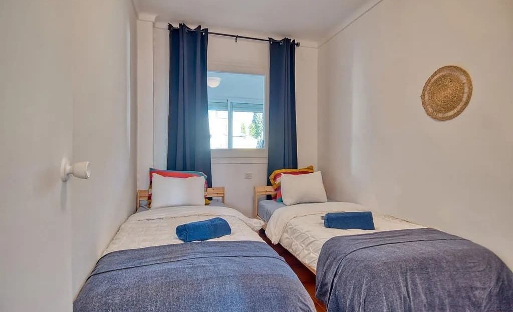 Спальня с двумя односпальными кроватями и окном с занавесками.