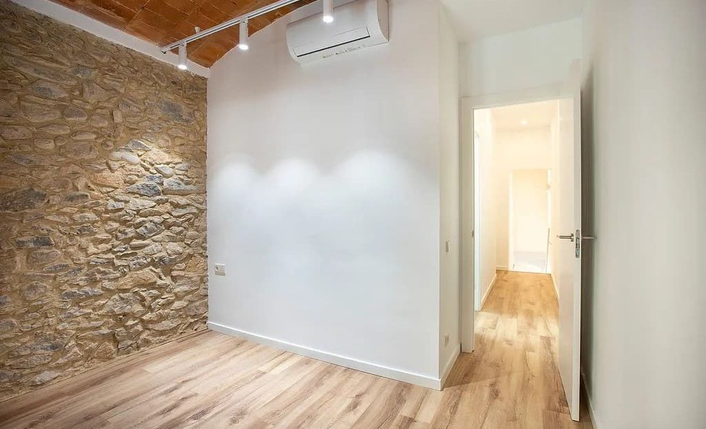 Комната с каменной стеной и деревянным полом, подготовленная под спальню или кабинет.