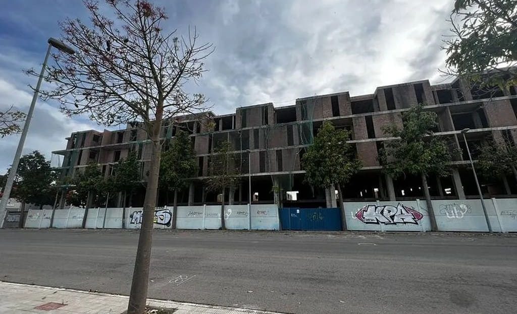 Недостроенное многоквартирное здание, вид с улицы за строительным забором.