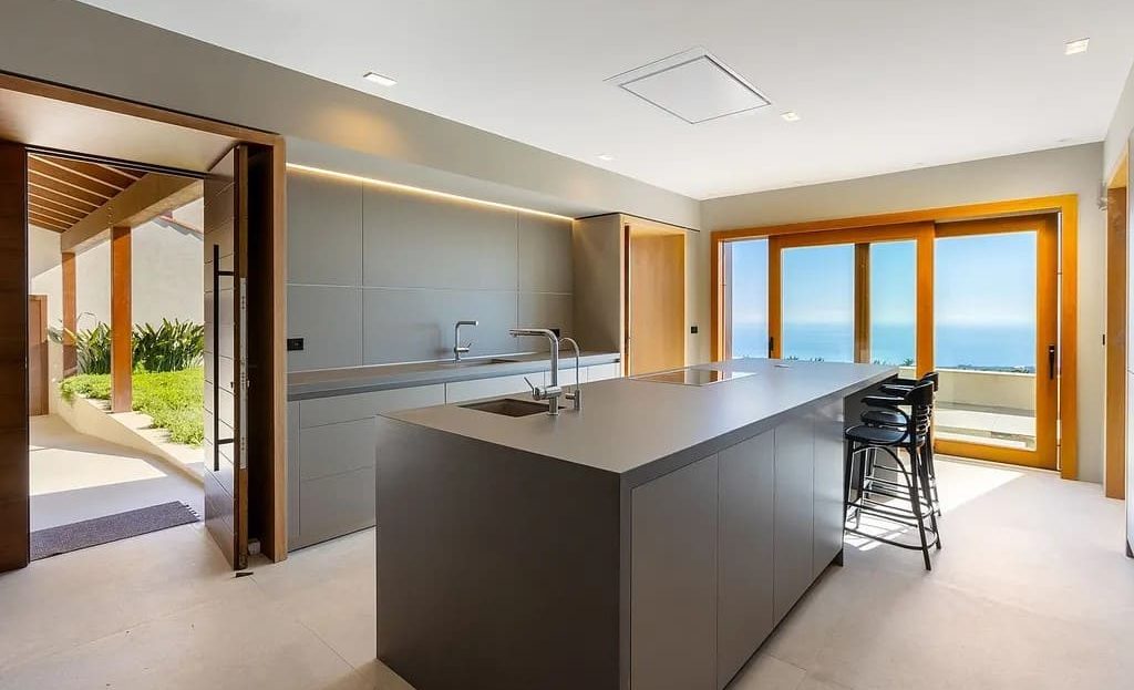 Современная кухня с островом и панорамными окнами с видом на море.