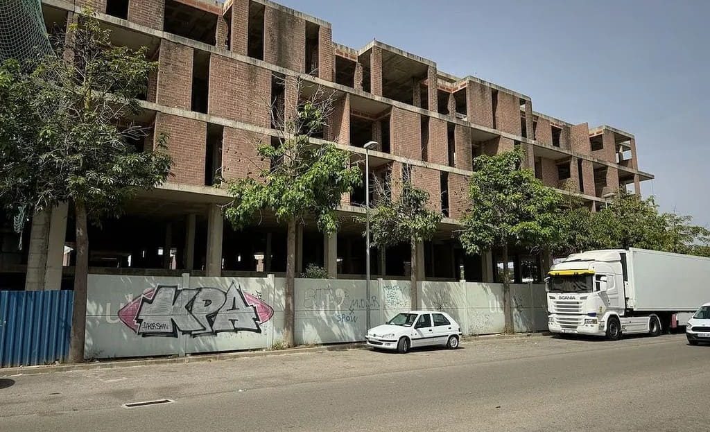 Фасад незавершённого жилого комплекса, вид спереди с припаркованными машинами.