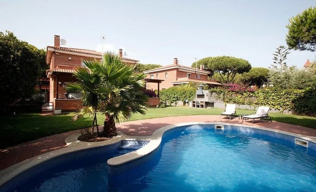 Бассейн на участке дома с зоной отдыха и зелёным садом.