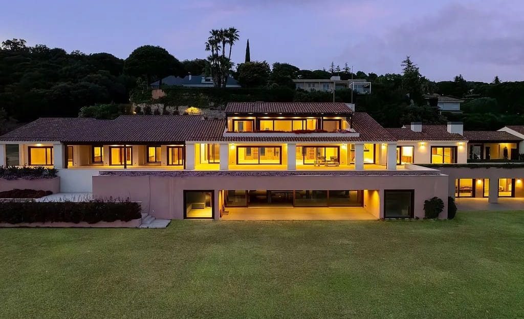 Фасад виллы на закате с подсветкой и видом на сад.