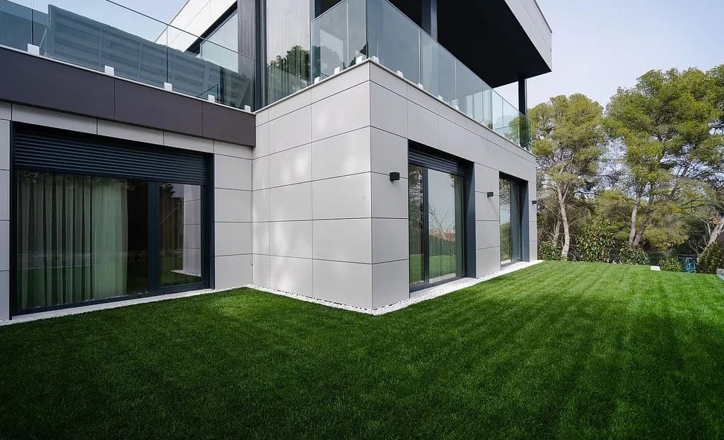 Фасад современной виллы с панорамными окнами и садом.