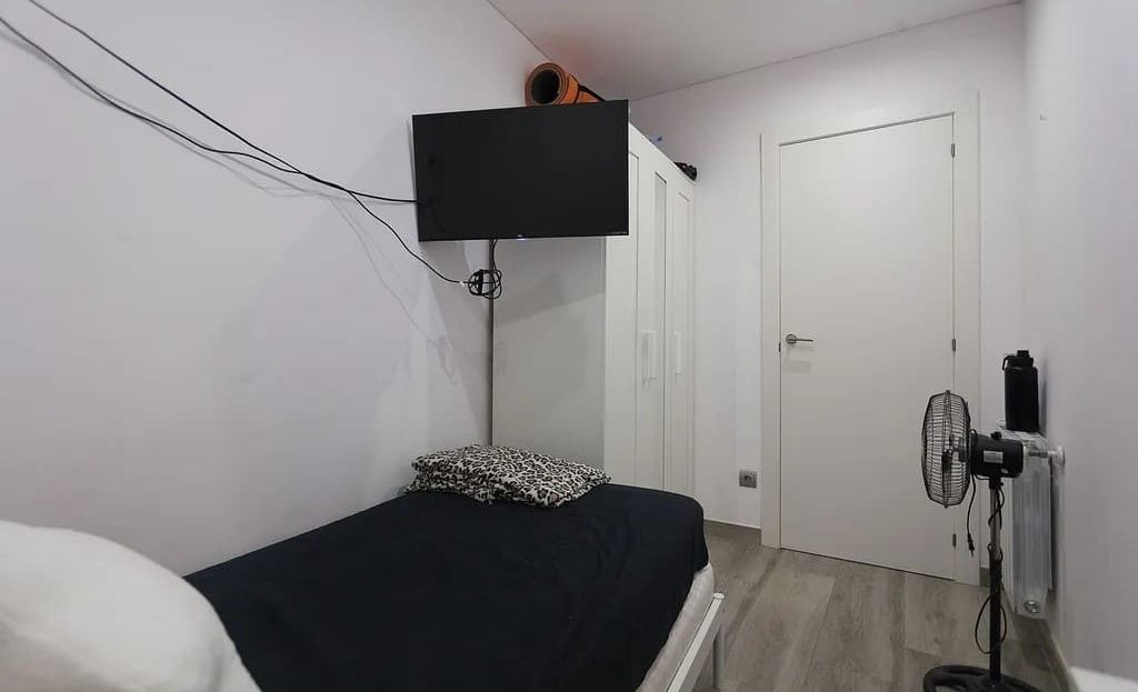 Спальня с односпальной кроватью и телевизором на стене.