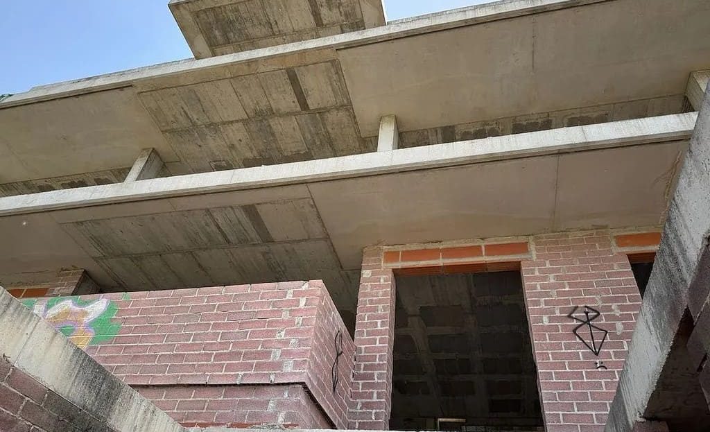 Вид на фасад с уровня земли, кирпичная кладка и несмонтированные проёмы.