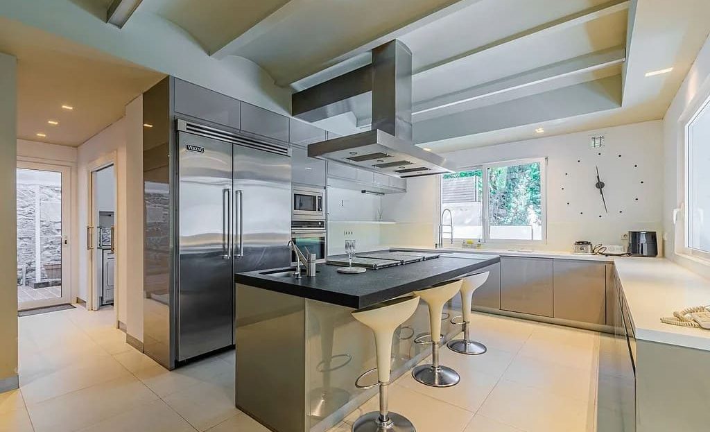 Современная кухня с островом, встроенной техникой из нержавеющей стали и выходом на террасу.