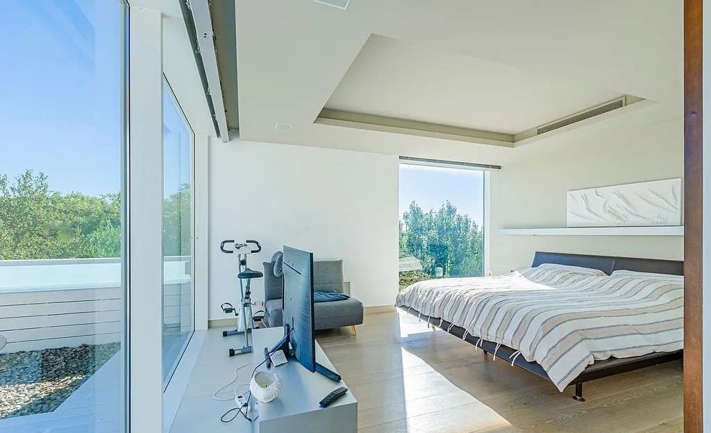 Главная спальня дома с панорамным остеклением, видом на Барселону и зоной для ТВ.