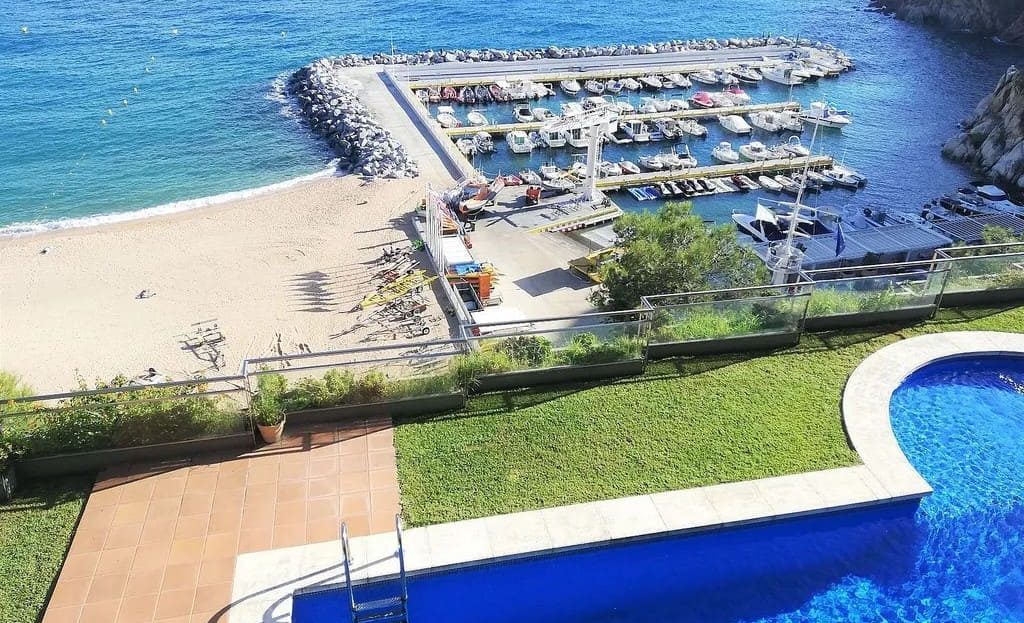 Лазурный бассейн на фоне песчаного пляжа и лодочного порта в Льорет-де-Мар.